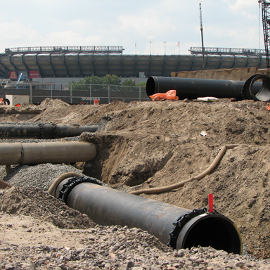 Precise bedding for new 30-inch DI pipe among and between existing utilities Construction of Met Life Stadium in East Rutherford, NJ - 2007. Old Giants Stadium the background has since been demolished.
